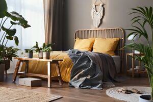 Ein Bett mit gelber Bettwäsche vor einer grauen Wand umgeben von Zimmerpflanzen
